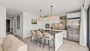 A modern kitchen with a central island, bar stools, pendant lighting, and stainless steel appliances.