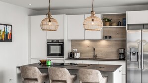 A modern kitchen with white cabinets, a stainless steel refrigerator, a built-in oven, and a central island with bar stools.