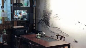 A dining area with a wooden table and chairs, a television on a shelf, and a mural on the wall. - Qiyue Linyin Bieyuan (Lijiang Gucheng Mufu Branch) (Lijiang)