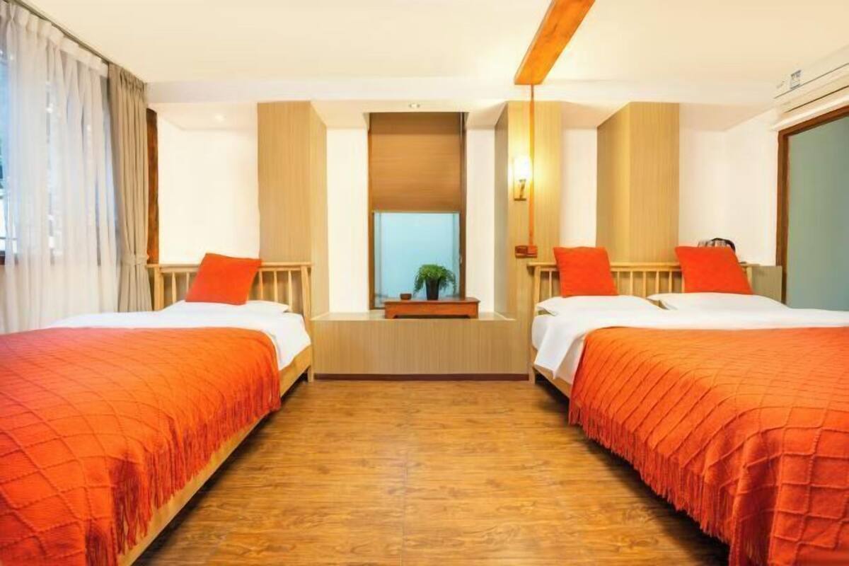 Une chambre d’hôtel avec deux lits, un plancher en bois, une fenêtre centrale et un miroir.