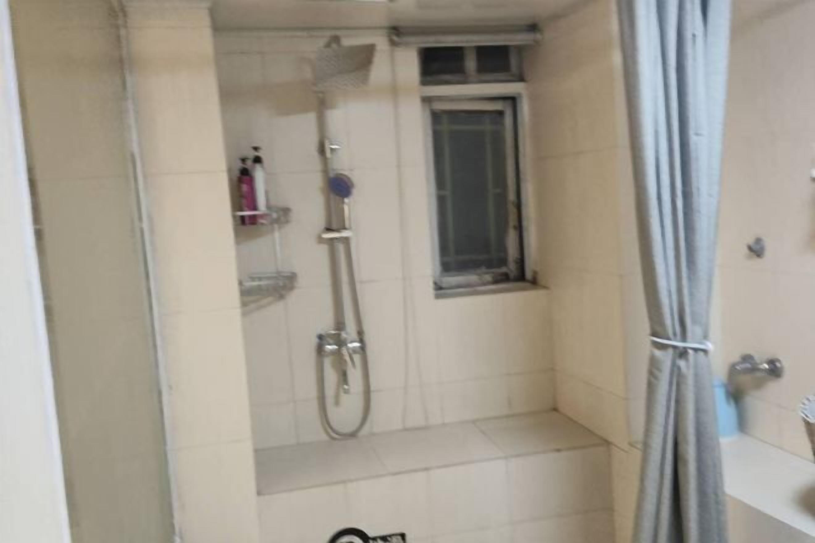 A small, tiled bathroom with a shower, a window, and a towel hanging on the wall.