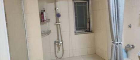 A small, tiled bathroom with a shower, a window, and a towel hanging on the wall.