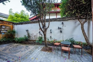 A courtyard with a tiled floor, a small round table with chairs, and a wall with decorative elements.