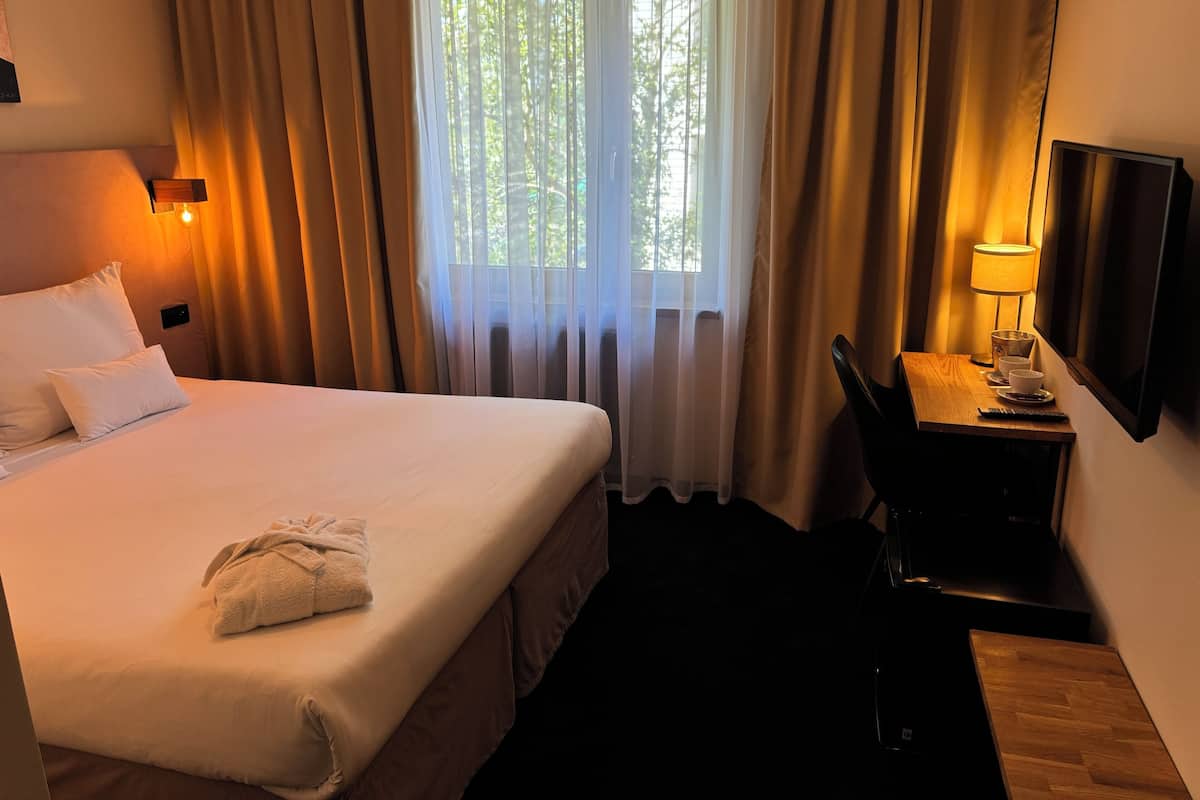 Ein Hotelzimmer mit Bett, Schreibtisch, Lampe und Fernseher.
