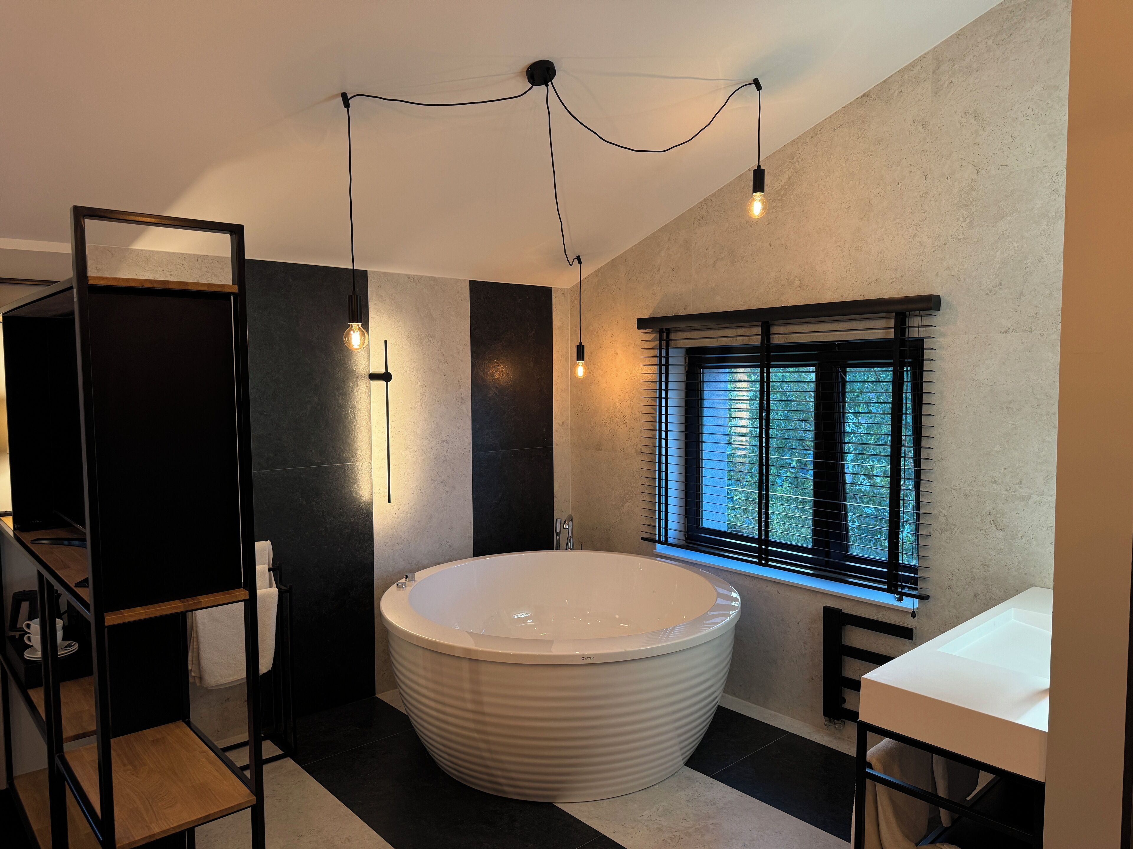 A modern bathroom with a freestanding bathtub, a vanity with a mirror, and a window with blinds.