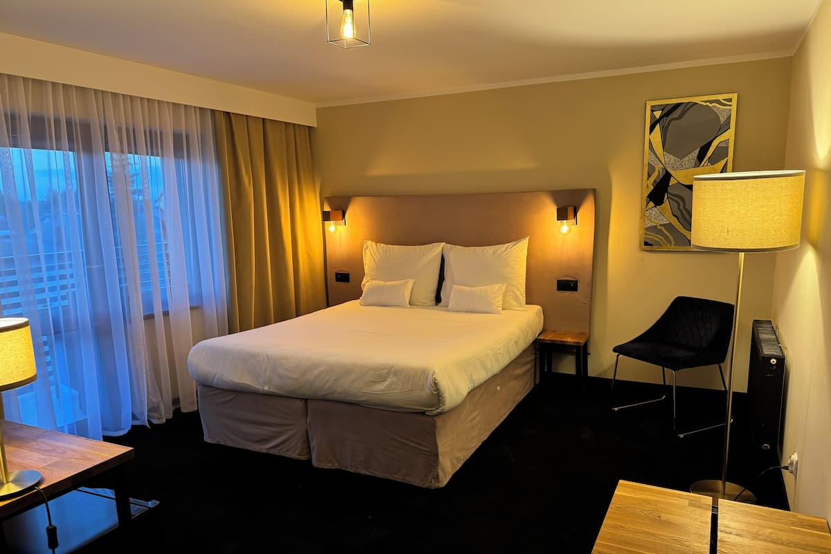 Ein Hotelzimmer mit einem großen Bett, einem Schreibtisch mit Lampe, einem Sessel und einem Nachttisch.