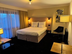 Ein Hotelzimmer mit einem großen Bett, einem Schreibtisch mit Lampe, einem Sessel und einem Nachttisch.