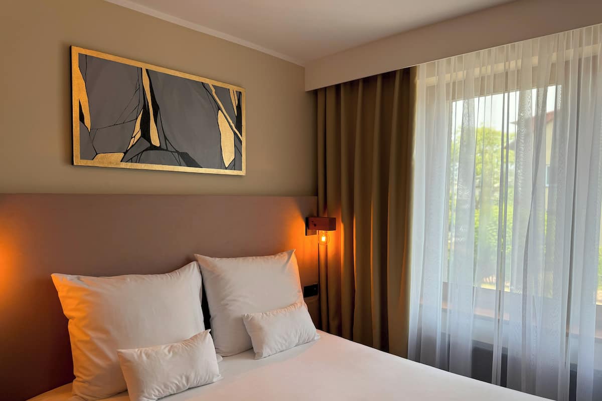 Ein Hotelzimmer mit einem großen Bett, einem Bild an der Wand und transparenten Vorhängen am Fenster.