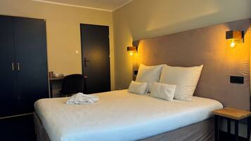 A hotel room with a large bed, bedside tables, a desk, and a wardrobe.