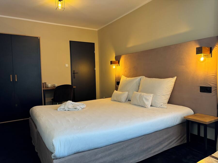 A hotel room with a large bed, bedside tables, a desk, and a wardrobe.