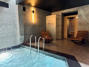 Ein Wellnessbereich mit Whirlpool, Holzbänken und einem an der Wand befestigten Schild für 'Amber Blue Wellness & Spa'.