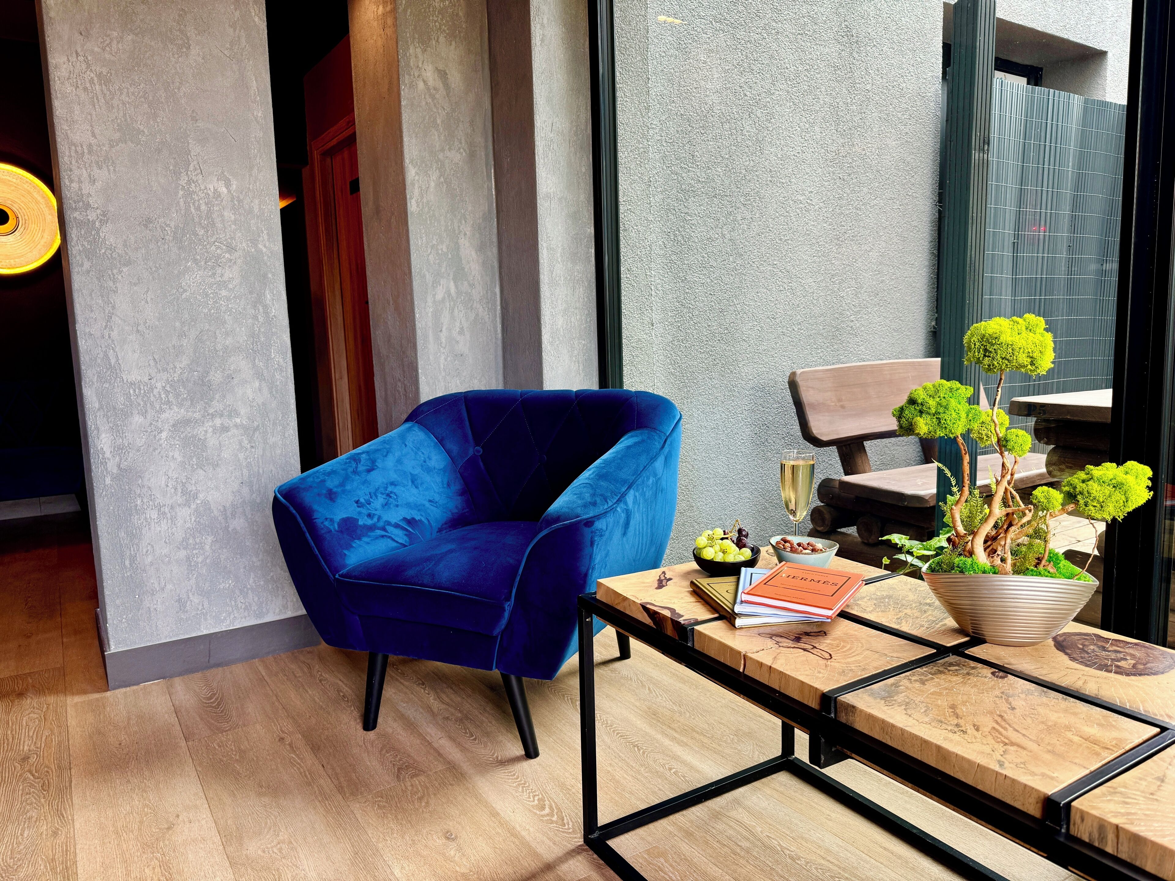 A modern room with a blue velvet chair, a wooden table with a potted plant, and a glass of champagne.
