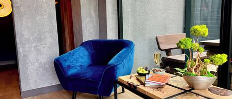 A modern room with a blue velvet chair, a wooden table with a potted plant, and a glass of champagne.