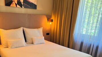 A neatly made bed with a folded robe, a modern abstract painting on the wall, and a window with sheer curtains.