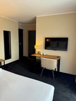 Una habitación de hotel con una cama, un escritorio con silla, un televisor y una cafetera.