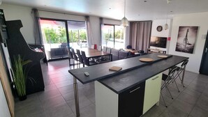 A modern kitchen with a central island, dining area with chairs, and a view to the outside. - Maison de Vacances Avec Piscine - La Maison des Lacs (Lesmont)