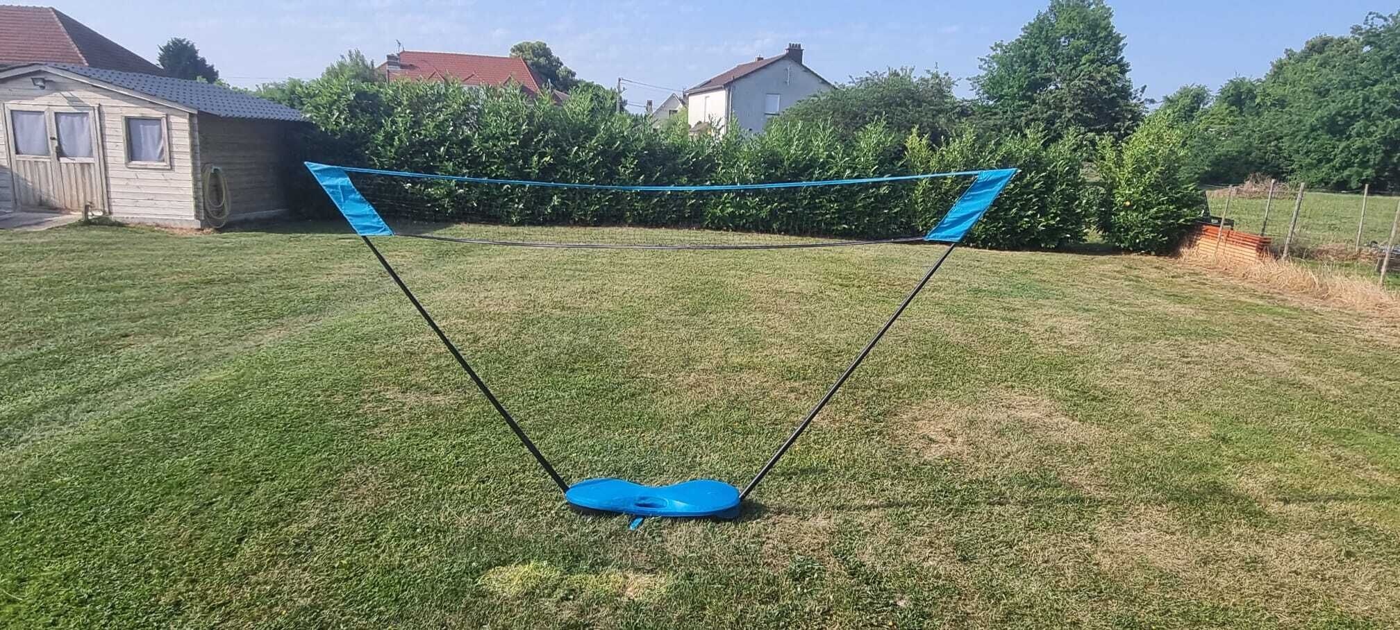 Een trampoline in een achtertuin met een huis en bomen op de achtergrond.