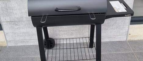 A black barbecue grill with wheels, positioned on a tiled floor against a tiled wall.