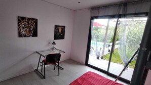 A room with a glass desk, a chair, a red bed, and two framed pictures on the wall. - Maison de Vacances Avec Piscine - La Maison des Lacs (Lesmont)