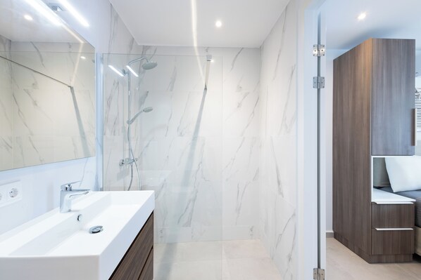 Un baño moderno con ducha de mármol, lavamanos blanco y muebles de madera.