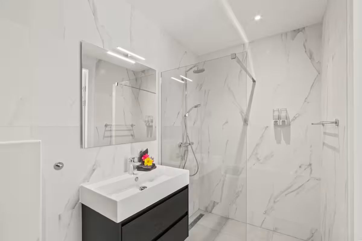 Een moderne badkamer met een wastafel van wit marmer, een grote spiegel en een douchecabine met glazen wanden.