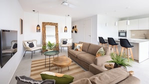 A modern living room with a sofa, chairs, a coffee table, and a dining area with stools. - The Breeze (Sint Michiel)