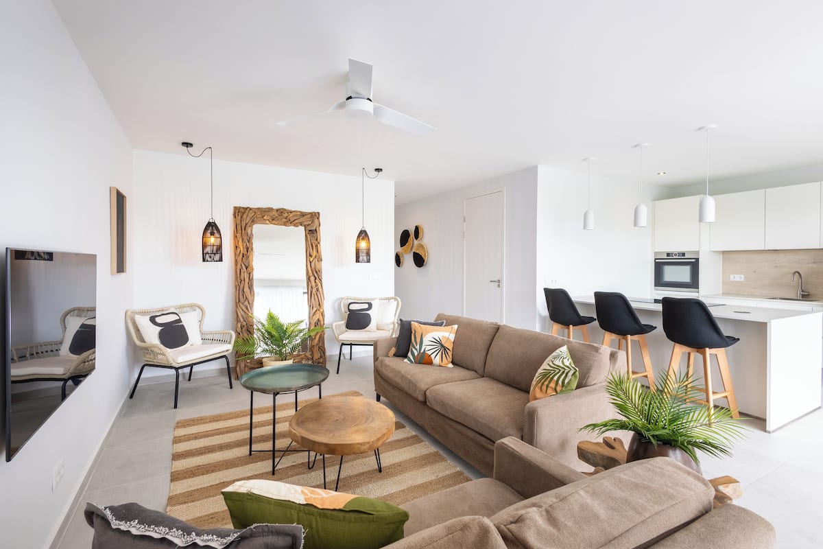Un salon moderne comprenant un canapé, des fauteuils, une table basse et un coin repas avec des tabourets.
