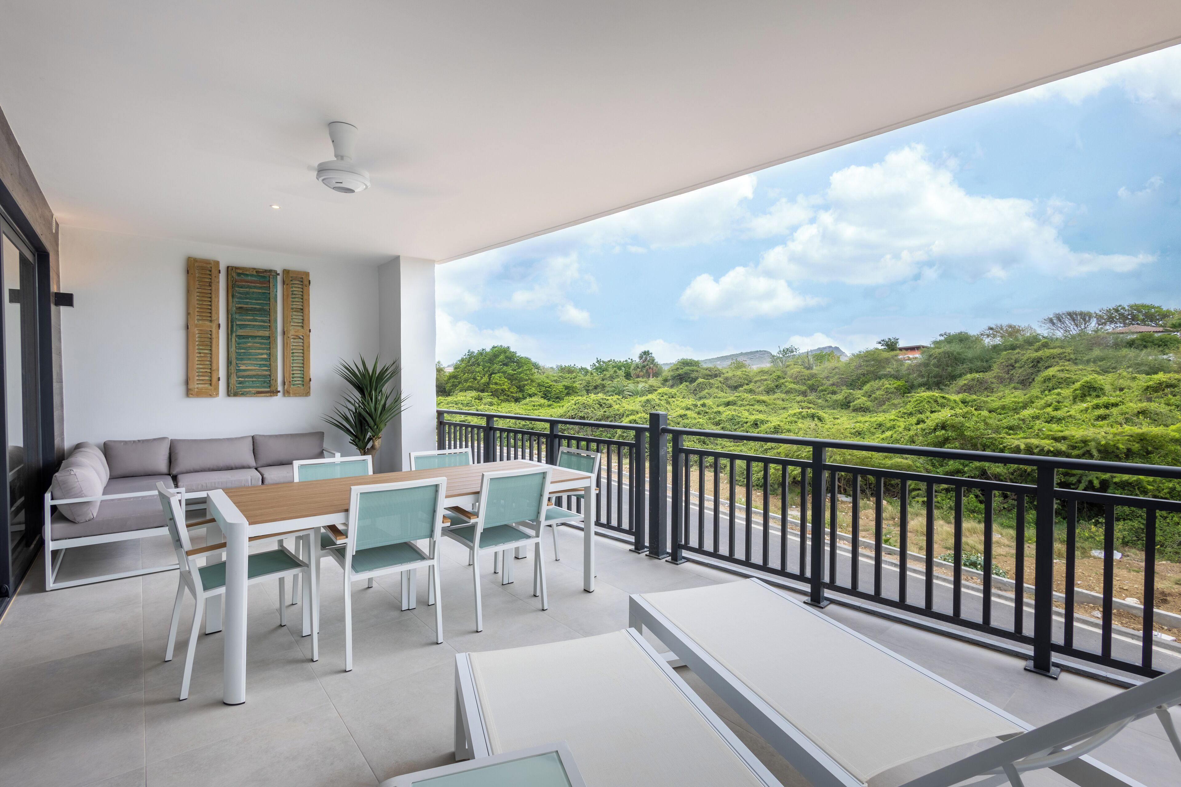 A balcony with a dining area, a sofa, and a view of greenery and buildings.