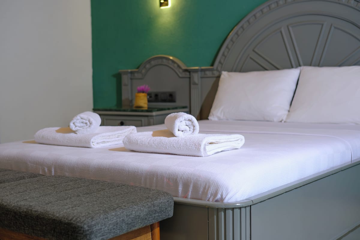 A neatly made bed with white linens and a grey bench in a room with teal walls.