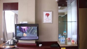 Zona de recepción de un hotel con un televisor, un certificado enmarcado en la pared y una vitrina de vidrio con botellas de agua.