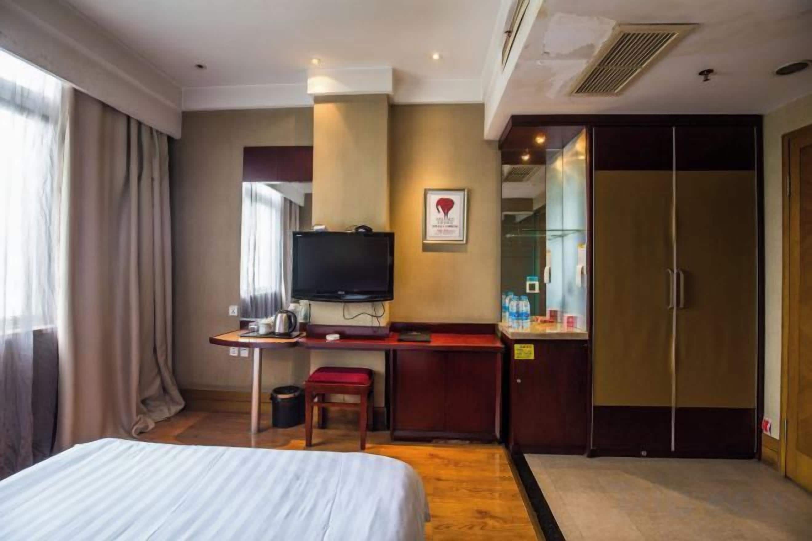 A hotel room with a bed, a desk with a television, a mirror, and a wardrobe.