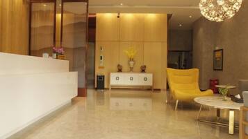 Zona de recepción con un mostrador blanco, un sillón amarillo y una mesa redonda con un jarrón de flores.