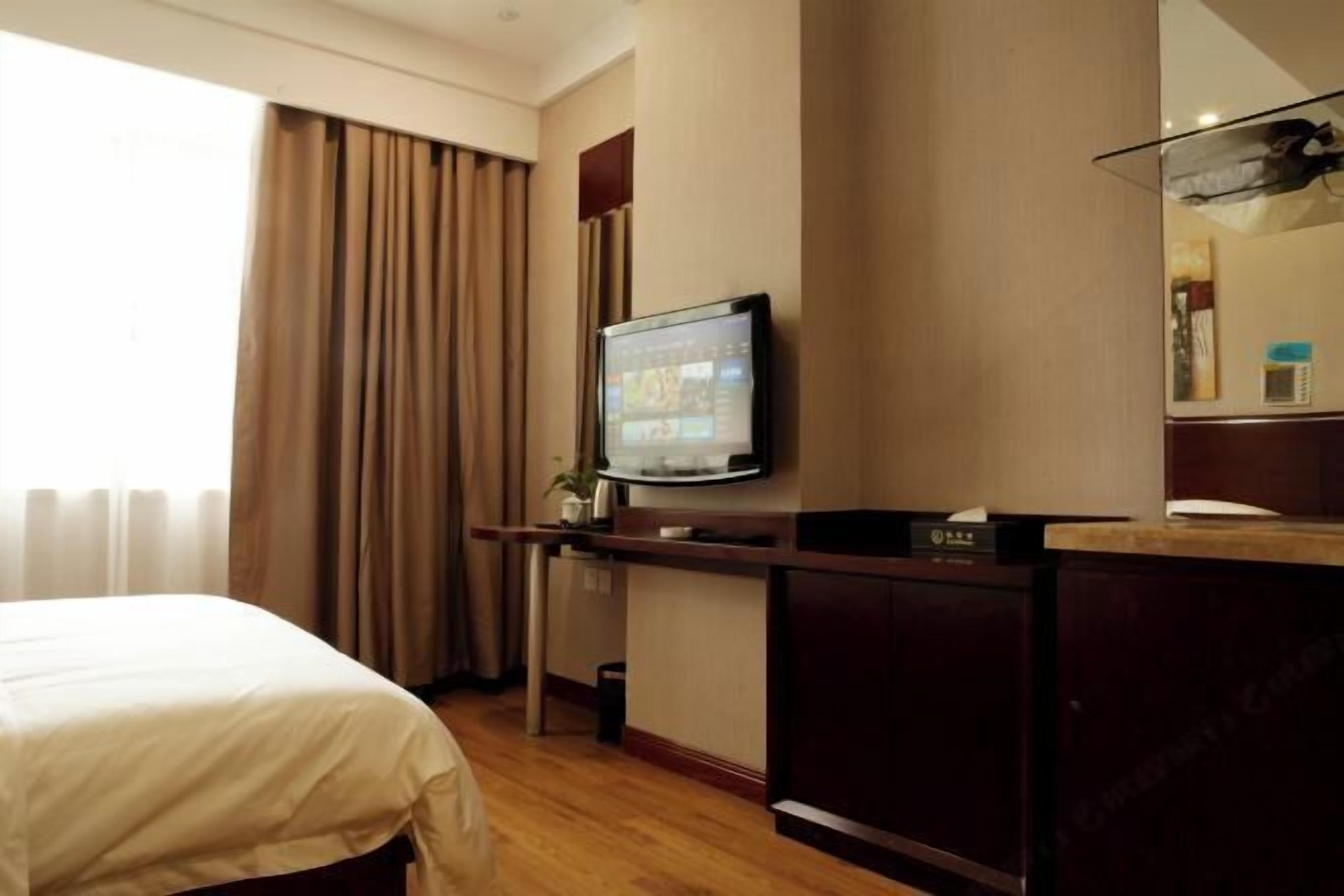 Une chambre d’hôtel avec un lit, un bureau avec une télévision et une grande fenêtre avec des rideaux.