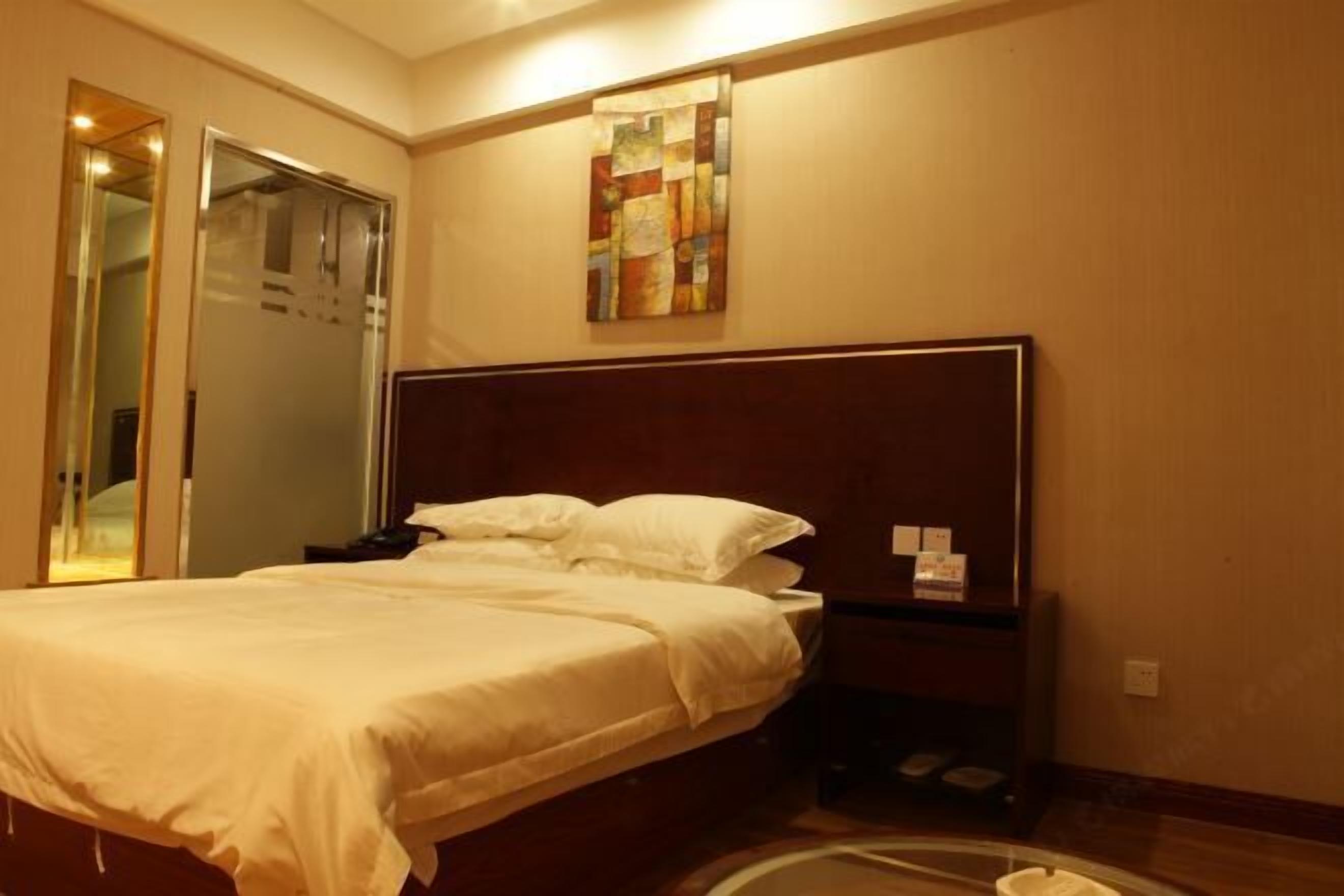 Ein Hotelzimmer mit einem Bett, einem Nachttisch, einem Kunstwerk an der Wand und einer Tür mit Spiegel.