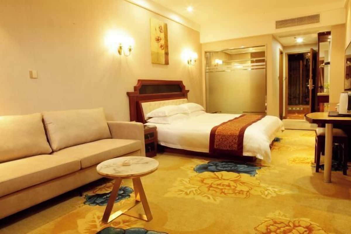 Habitación de hotel con cama, sofá, una mesita redonda y alfombra estampada con motivos florales.