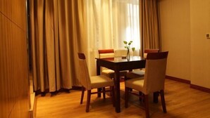 Un coin repas avec une table et des chaises en bois, un vase rempli de fleurs et une vue à travers des rideaux légers.