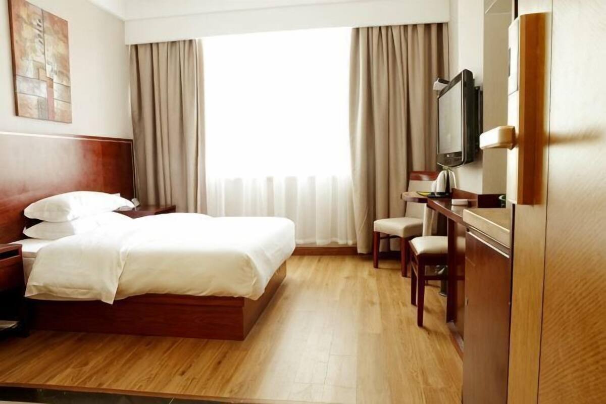 Una habitación de hotel con cama, escritorio, silla, televisor y ventana con cortinas.