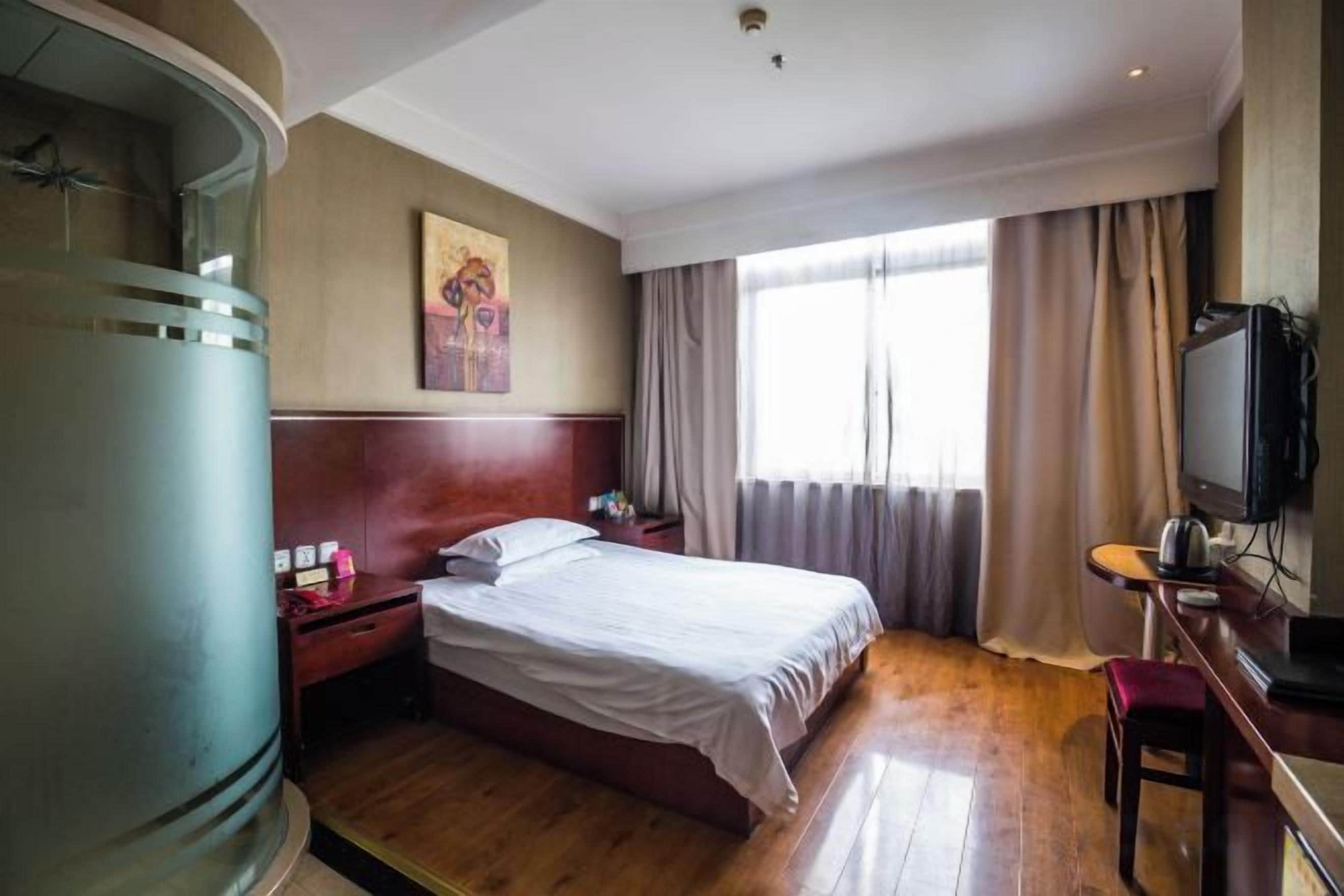 Een hotelkamer met een bed, een bureau met stoel, een televisie en een groot raam met gordijnen.
