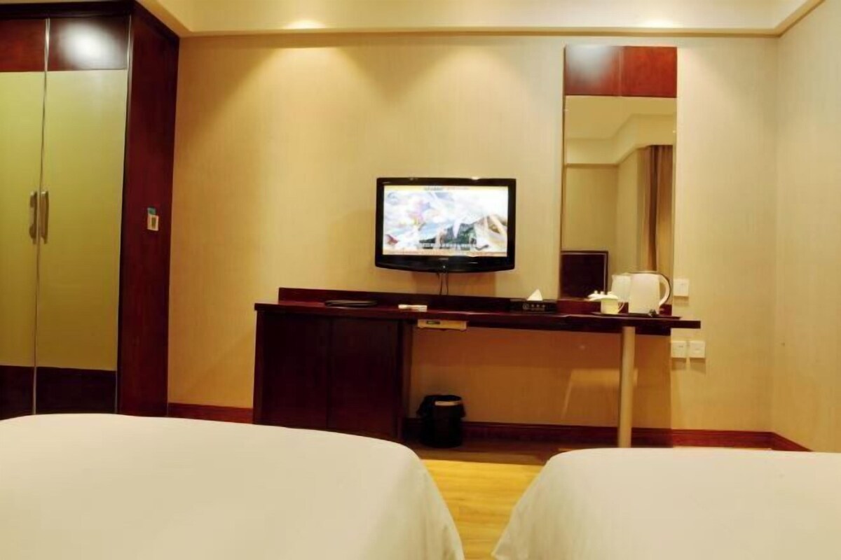 A hotel room with two beds, a TV on a desk, a mirror, and a wooden wardrobe.