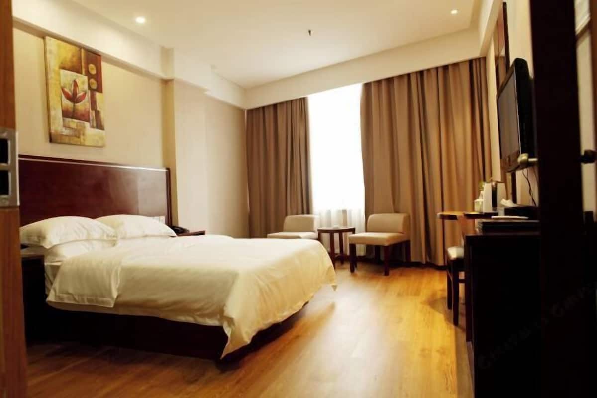 Habitación de hotel con cama, escritorio, silla, televisión y ventana con cortinas.