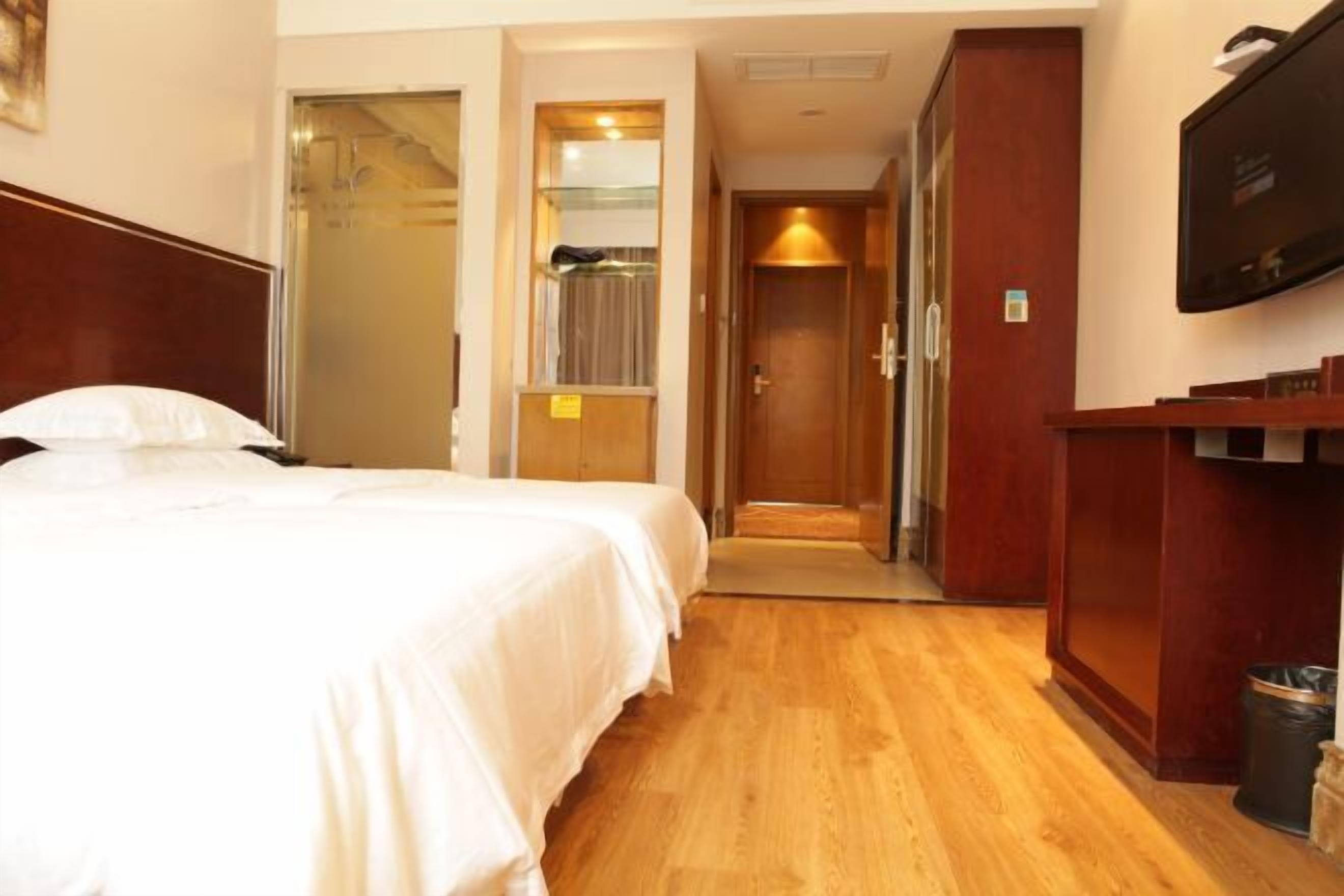 Ein Hotelzimmer mit Bett, Holzboden, Fernseher und einem Flur, der zu einem Badezimmer führt.