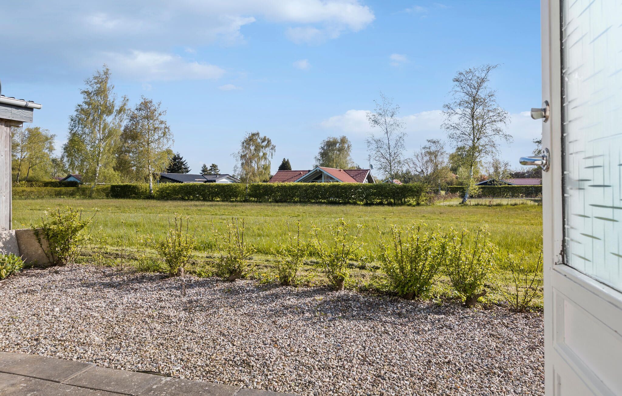 A residential area with a gravel driveway, a grassy field, and houses with red roofs.