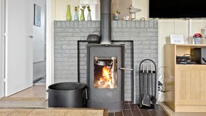 Un salon moderne avec une cheminée en pierre, un poêle noir et un petit pot noir placé à côté.