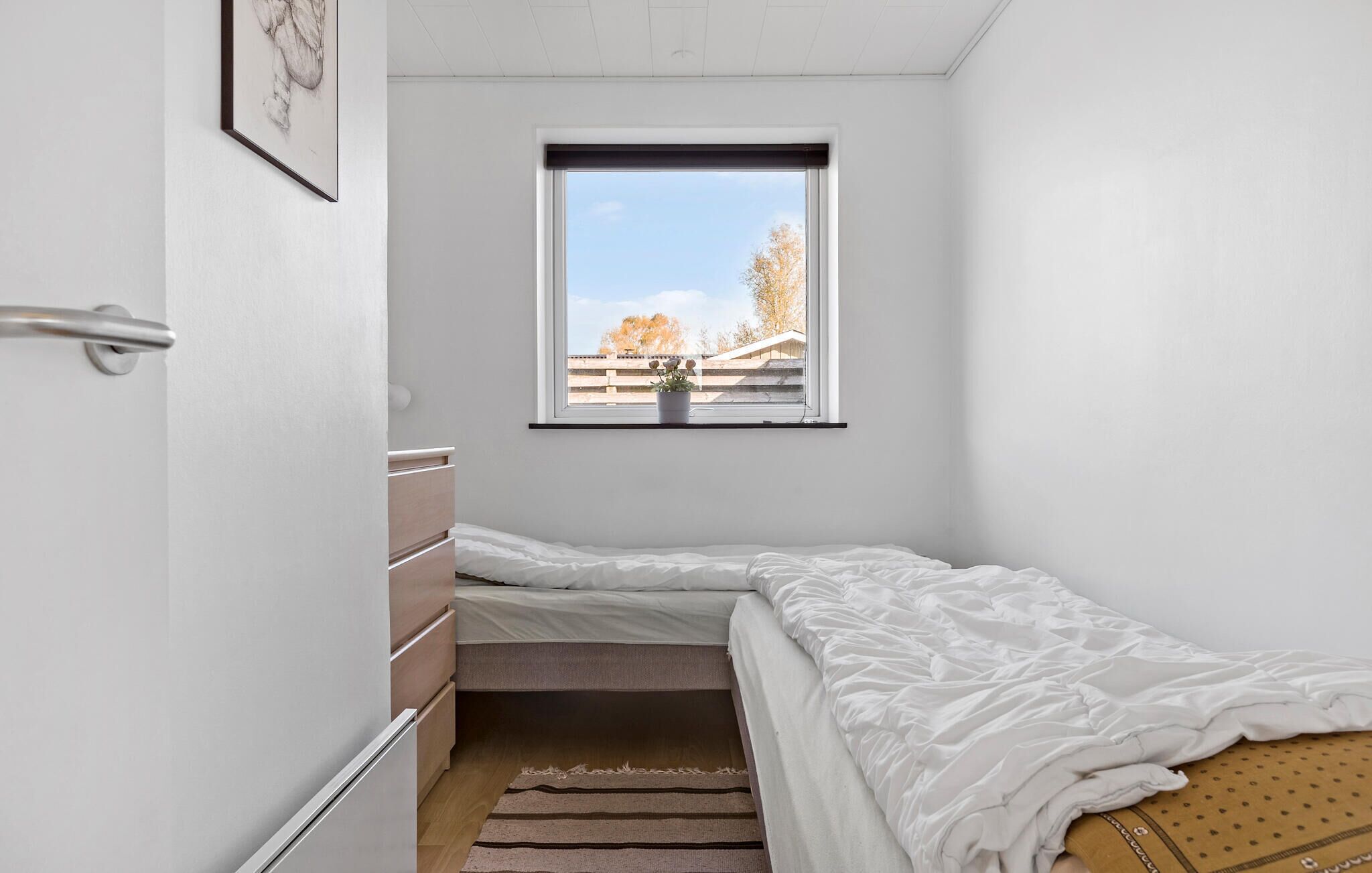 A small, single-bed room with a window offering a view of trees and a fence.