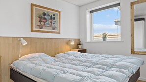 Une chambre à coucher avec un lit, une table de chevet, une lampe, une fenêtre donnant sur un beau paysage et un tableau encadré au mur.