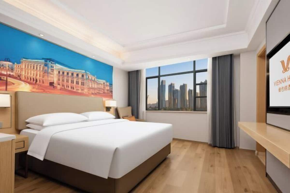 A hotel room with a large bed, a cityscape view, a desk, and a TV screen.