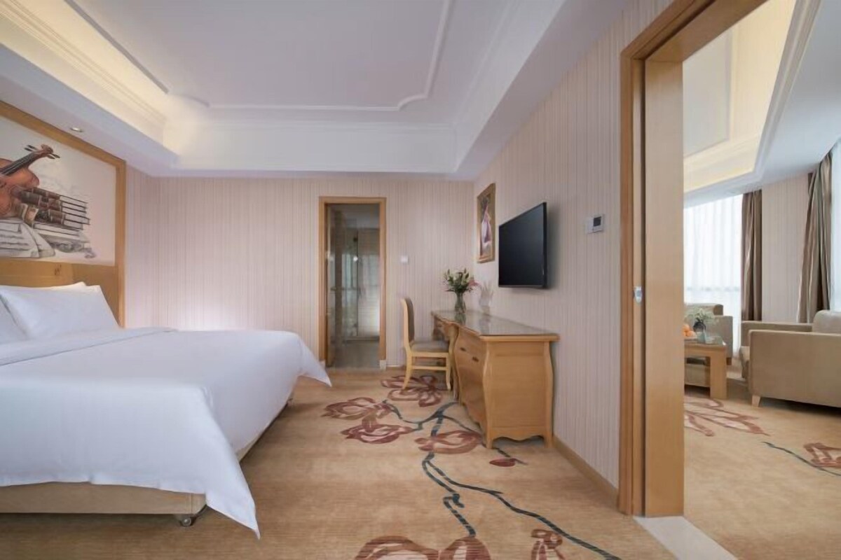 Ein Hotelzimmer mit einem Bett, einem Schreibtisch, einem Sessel, einem Fernseher und einer Tür zu einem weiteren Raum.