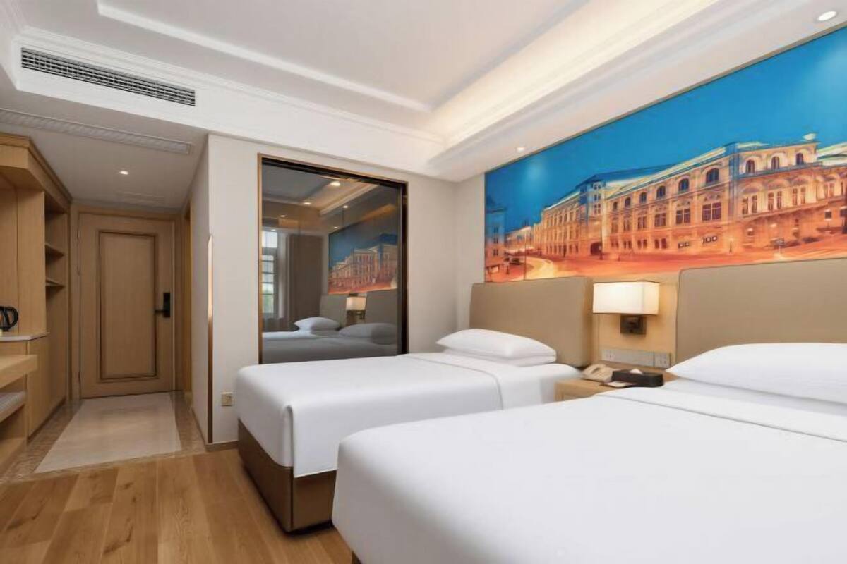 A hotel room with two beds, a painting of a building, a wooden cabinet, and a door leading to another room.