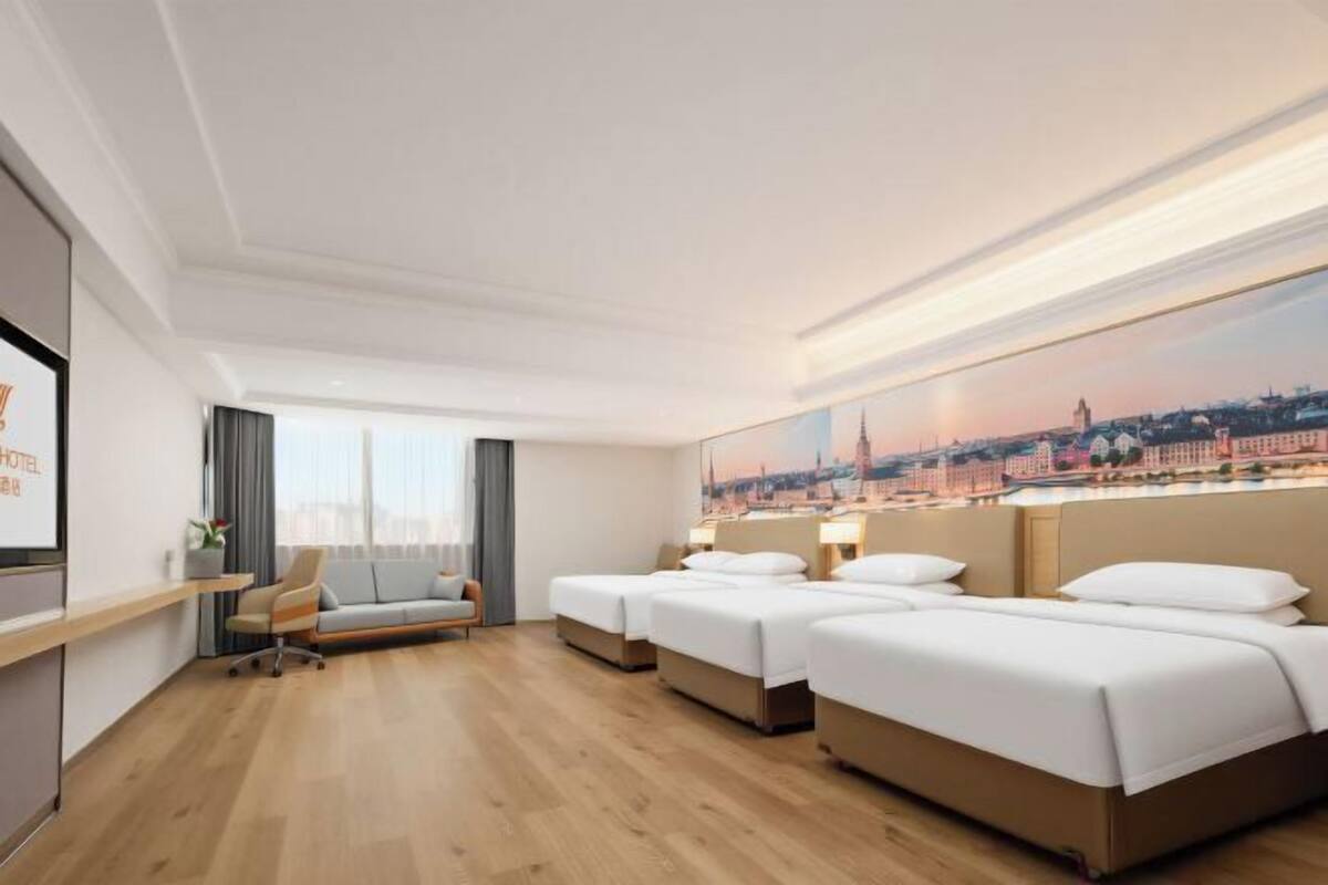 A hotel room with three beds, a desk, a chair, and a large window.