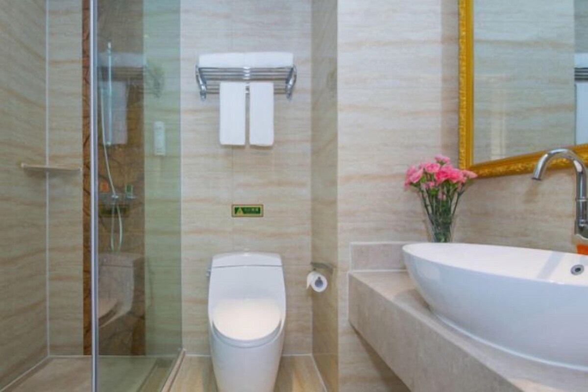 Ein modernes Badezimmer mit Duschkabine aus Glas, Toilette, Waschbecken mit Blumenvase und Spiegel mit goldener Rahmung.